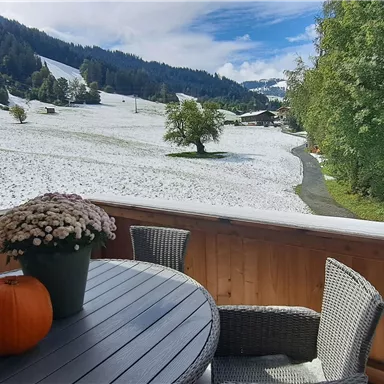 A beautiful terrace with a round table and a pumpkin. In the background, snowy meadows and green trees can be seen.