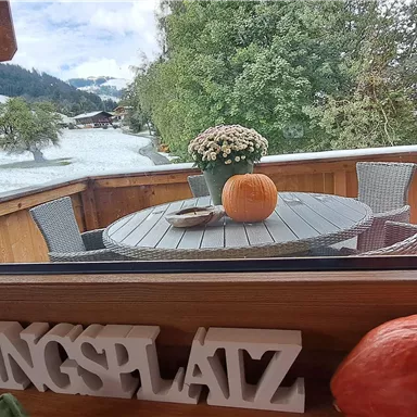 A cozy view out the window onto a terrace with a table and chairs. In the foreground are a pumpkin and a flower vase.