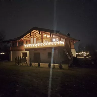 A cozy house with warm lights, illuminated at night. The surroundings are dark and quiet.