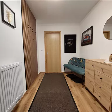 Ein moderner Flur mit warmen Holztönen und einem gemütlichen Sitzbereich. An der Wand hängen Bilder, und ein runder Spiegel ist sichtbar.