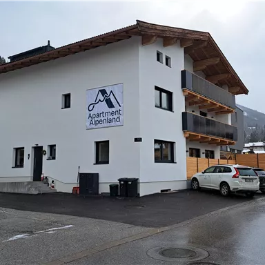 Ein modernes Gebäude mit der Aufschrift "Apartment Alpenland". Es befindet sich in einer ruhigen Umgebung, umgeben von Bergen.