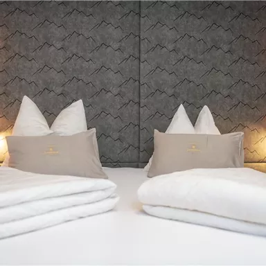 Ein gemütliches Schlafzimmer mit zwei Einzelbetten und schönen Kissen. Die Wände sind in einem modernen Muster gehalten, mit sanften Lichtquellen an beiden Seiten.