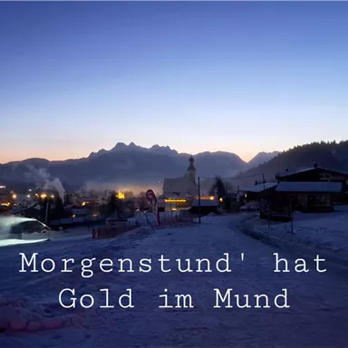 A quiet winter landscape at dusk with snow-covered mountains. Illuminated houses are visible in the background.