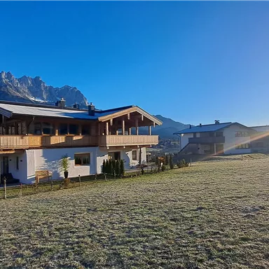A beautiful house in a rural setting with mountains in the background. The sun is shining and the sky is clear.