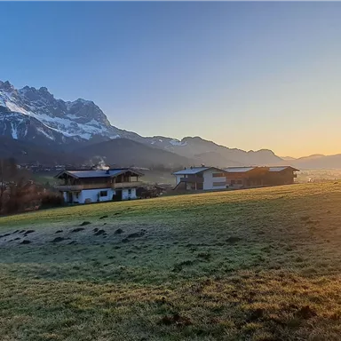 A beautiful landscape with mountains and a sunrise. In the foreground, there is lush green and some houses.