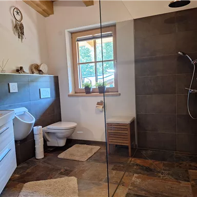 A modern bathroom with a glass shower and stylish tiles. It features a sink, a toilet, and a window with natural light.