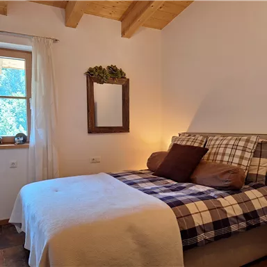 A cozy bedroom with a double bed, a window, and a wooden frame. The decor is warm and inviting, with a soft color tone.