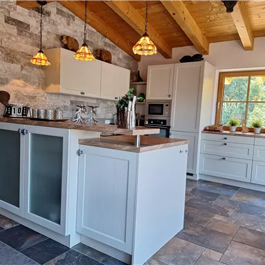 A modern kitchen with a wooden ceiling and stone wall. The space is bright and inviting with plenty of storage and stylish details.
