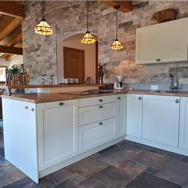 A modern kitchen with white cabinets and woodwork. The floor is made of dark tiles and the lighting creates a cozy atmosphere.