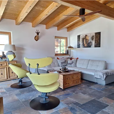 A modern living room with wooden ceilings and tiled floors. There is a bright couch, striking yellow armchairs, and decorative elements on display.
