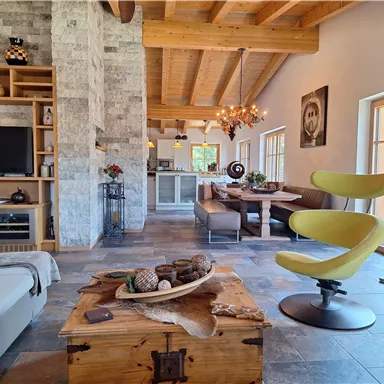 A modern living room with wooden ceilings and a cozy dining nook. The decor is stylish and inviting, with plenty of natural light.