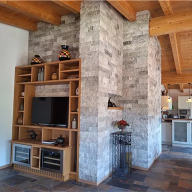 A stylish living room with a modern stone wall and a TV unit. The open space features wooden beams and an inviting atmosphere.