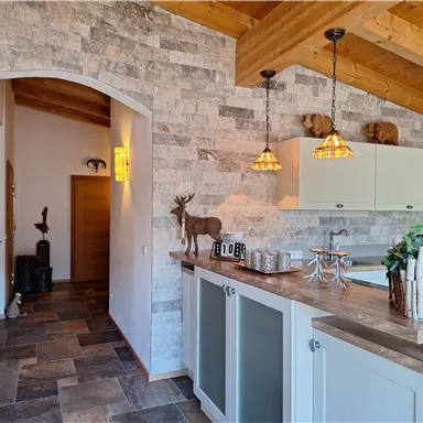 A modern kitchen with wooden elements and a cozy atmosphere. The walls are clad in stone, and soft lighting provides inviting light.