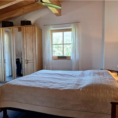 A bright bedroom with a large bed and wooden details. The room has large windows that let in plenty of daylight.