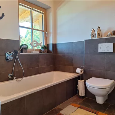 A modern bathroom with a bathtub and a toilet. The walls are painted in neutral tones, and there are windows with plenty of natural light.