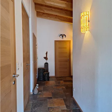 A bright hallway with wooden ceilings and stone tiles. Several doors and decorative elements create an inviting atmosphere.