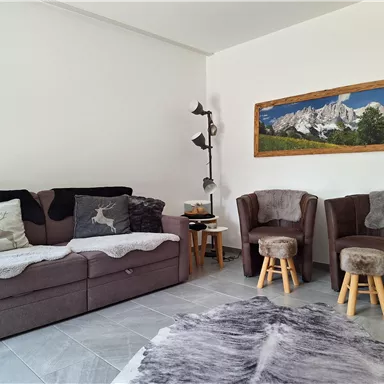 A modern living room with a comfortable sofa and two armchairs. On the wall hangs a picture of a mountain landscape.