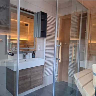 A modern bathroom with a glass shower and an elegant sink. Wooden details and soft lighting create a cozy atmosphere.