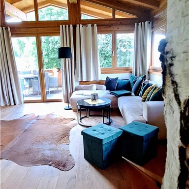 A cozy living room with wooden ceilings and large windows. The furniture is modern and colorful, with a beautiful view of nature outside.