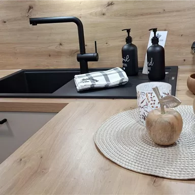 Eine moderne Küchenzeile mit Holzoberflächen und minimalistischer Ausstattung. Auf dem Tisch sind dekorative Gegenstände wie eine Schale, Kerzen und eine Kaffee Maschine zu sehen.