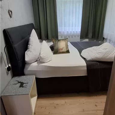 Ein gemütliches Schlafzimmer mit einem Doppelbett und großen Fenstern. Die Wände sind in sanften Farben gehalten und es gibt Holzfußboden.