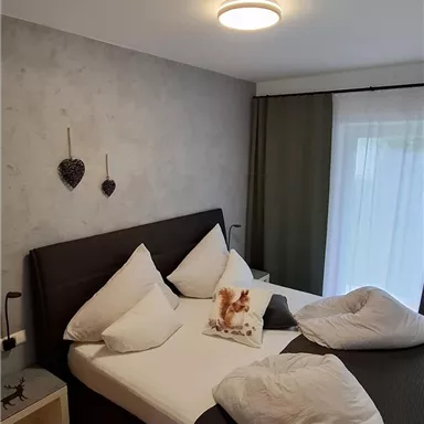 Ein gemütliches Schlafzimmer mit einem großen Bett und modernen Kissen. Die Wände sind neutral gehalten, und ein Fenster sorgt für Tageslicht.
