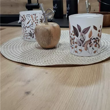 Ein schöner gedeckter Tisch mit einem runden Platzset. Auf dem Tisch stehen zwei dekorative Tassen und ein kleiner Holzapfel.