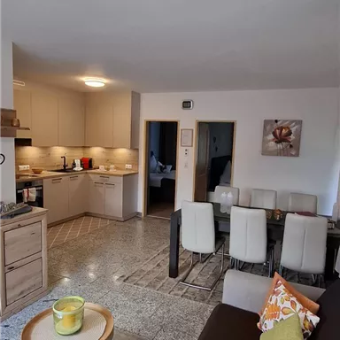 Ein modernes Wohnzimmer mit einer offenen Küche und einem Essbereich. Die Einrichtung ist hell und einladend mit einem bequemen Sofa und einem kleinen Tisch.