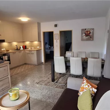 Eine moderne Wohnung mit einem offenen Wohn- und Essbereich. Die Küchenzeile und der Esstisch sind gut möbliert und schaffen eine einladende Atmosphäre.