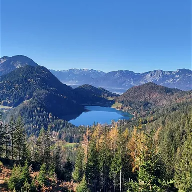 A picturesque mountain landscape with a clear lake in the middle. Surrounded by green forests and blue sky.