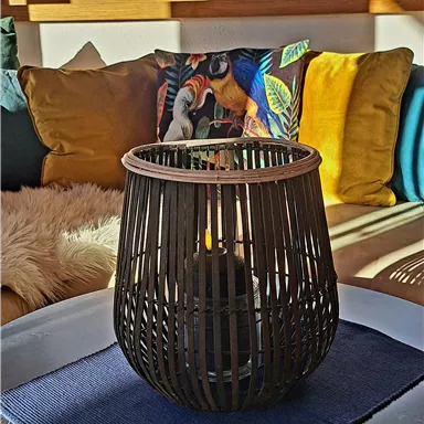 A stylish candle holder stands on a table in a cozy room. In the background, colorful cushions and a beautiful view of snow-covered mountains can be seen.
