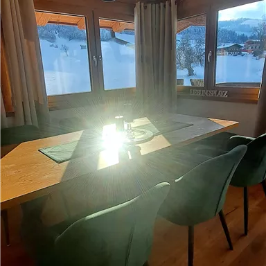 A cozy dining area with a large table and modern chairs. The window offers a beautiful view of the snowy landscape.
