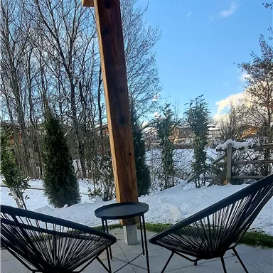 A cozy terrace with two black steel chairs and a small table. In the background, snow-covered landscapes and trees can be seen.