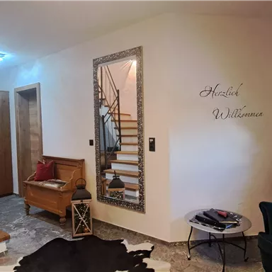 An inviting entrance area with a staircase and a cozy armchair. On the wall is the inscription "Welcome".