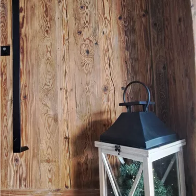 A cozy corner with a wooden wall and a decorative lantern. The lantern contains plants and stands on a wooden floor.