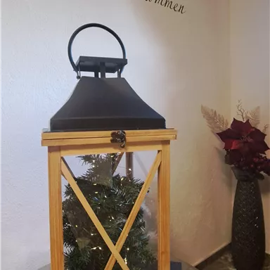 A beautiful wooden lantern stands on a table. Above it on the wall, it says "Welcome".