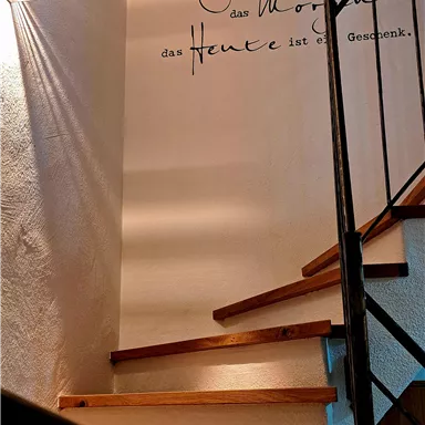 An elegant staircase leads up, illuminated by a wall lamp. An inspirational quote is written on the wall.