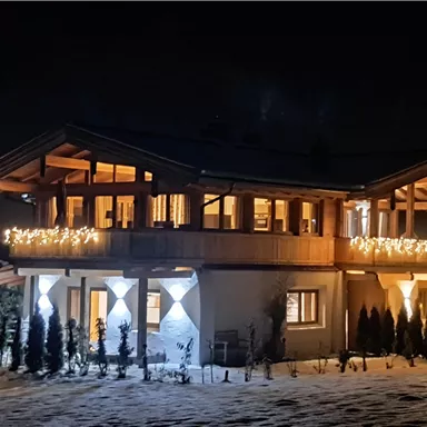 A brightly lit house in a snowy environment at night. The festive lighting creates a cozy atmosphere.