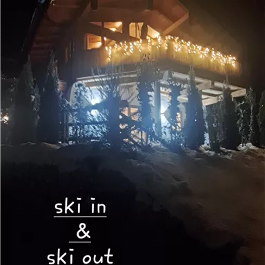 A cozy chalet at night, illuminated with lights. Access to the ski area is directly possible from the accommodation.