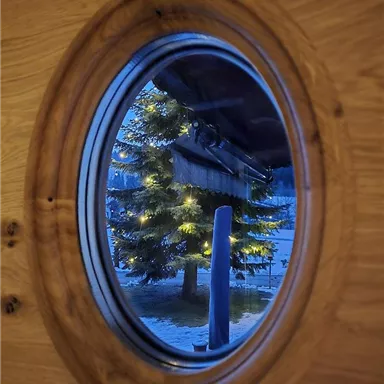 A round cutout shows a illuminated Christmas tree in front of a wooden house. The surroundings are bathed in soft blue.