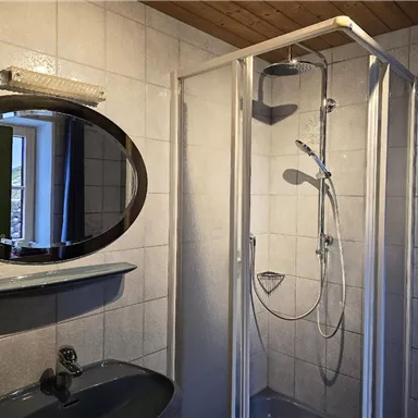 A modern bathroom with a shower and a sink. A round mirror is hung on the wall.