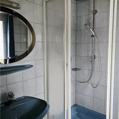 A modern bathroom with a shower cabin and a sink. The tiles are light gray, and there is a mirror over the sink.