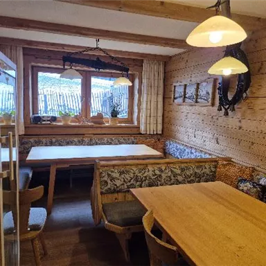 Ein gemütlicher Raum mit Holzwänden und mehreren Tischen. Die Fenster lassen viel Licht hereinf fallen und Pflanzen sorgen für eine einladende Atmosphäre.