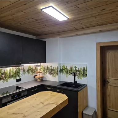 Eine moderne Küche mit schwarzen Schränken und einem großen Holztisch. An der Wand sind Pflanzenmuster dekoriert, die für eine frische Atmosphäre sorgen.