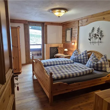 Ein gemütliches Schlafzimmer mit Holzmöbeln und einem großen Bett. Große Fenster lassen natürliches Licht herein und sorgen für eine einladende Atmosphäre.