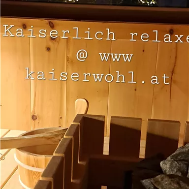A cozy sauna area with wooden interiors and stones. In the background, majestic mountains can be seen at dusk.