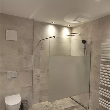 A modern bathroom with a walk-in shower and a clean design. The walls are painted in light colors, and the floor is made of gray stone.