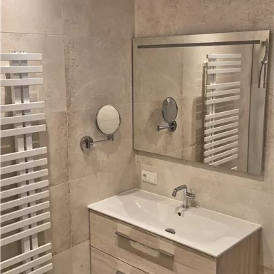 A modern bathroom with a wooden washstand and a large mirror. On the wall, there is a towel warmer.