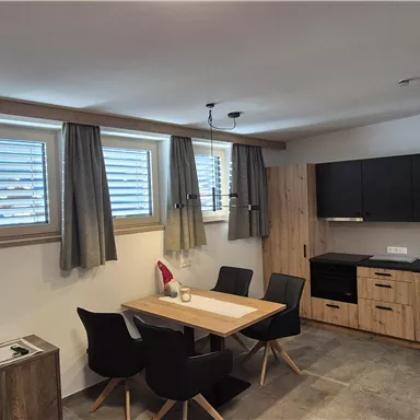 A modern kitchen with a dining area in a cozy room. Wooden furniture and a large wall with windows create a bright atmosphere.