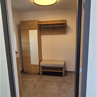 A bright entrance area with a piece of furniture for coats and a place to sit. The floor is decorated with a carpet.